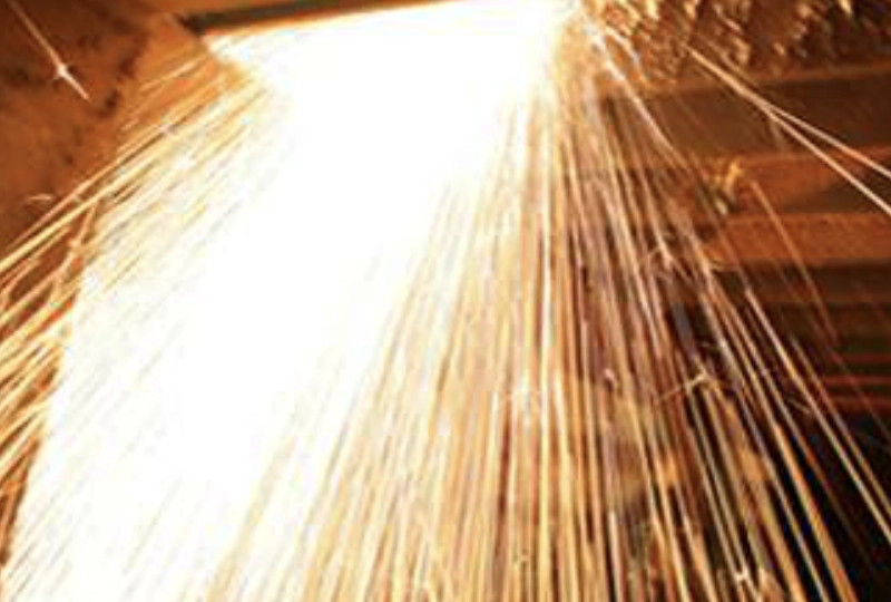 Close-up of bright orange and yellow sparks flying in multiple directions from a welding process.